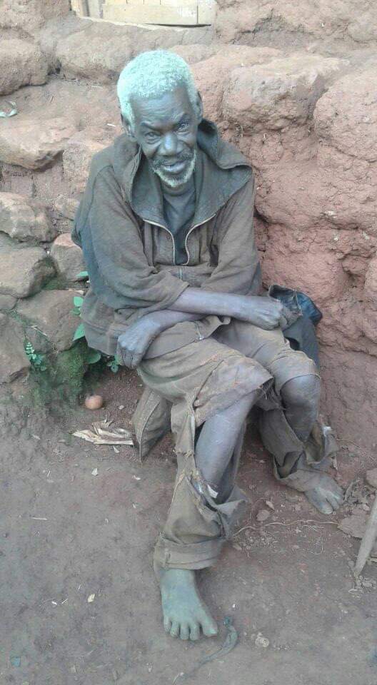 VISION old barefoot african man sitting on a bench in front of a stone building